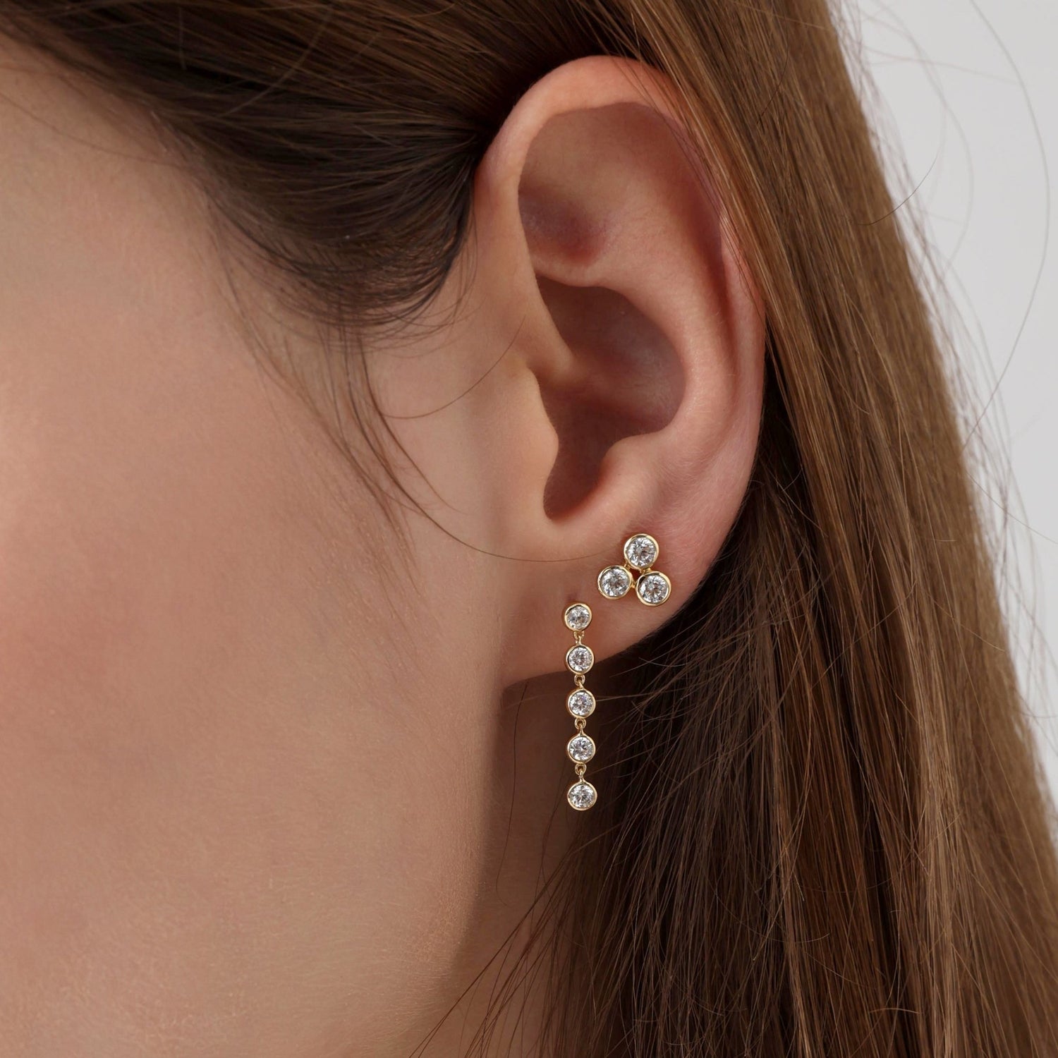 Close-up of an ear wearing a gold and diamond earring with a neutral background