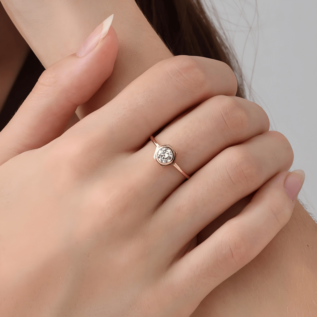Rose gold ring with a diamond on a person's finger against a neutral background
