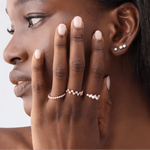 Close-up of a woman's hand with diamond rings and earrings against a neutral background