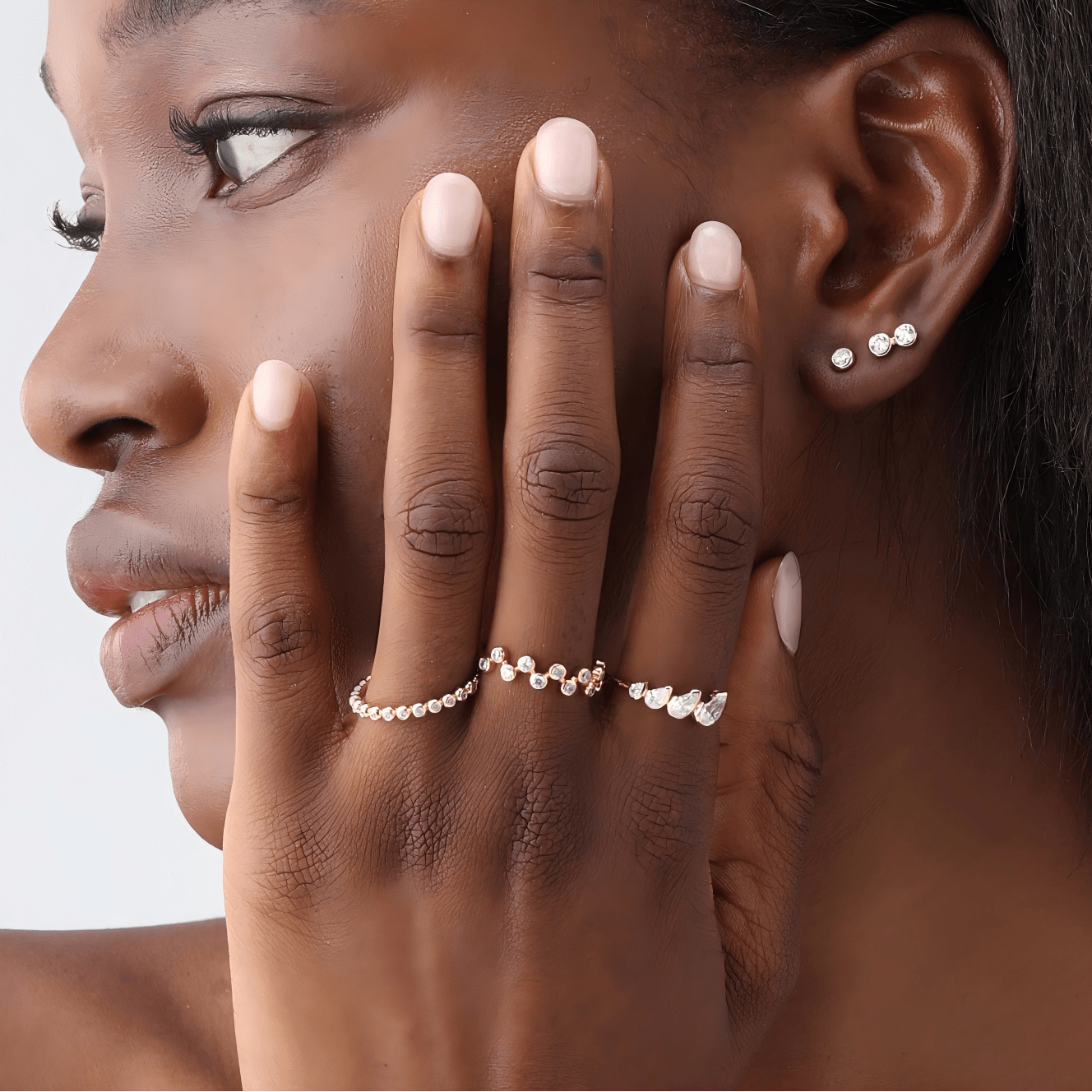 Close-up of a woman's hand with diamond rings and earrings against a neutral background