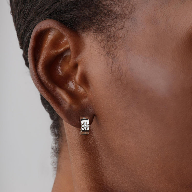 Close-up of an ear wearing a white gold clover hoop earring on a neutral background