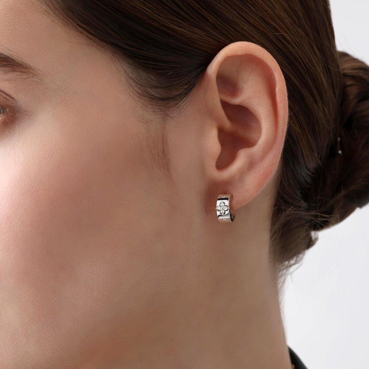 Close-up of a person wearing a white gold and diamond  hoop earring on a neutral background