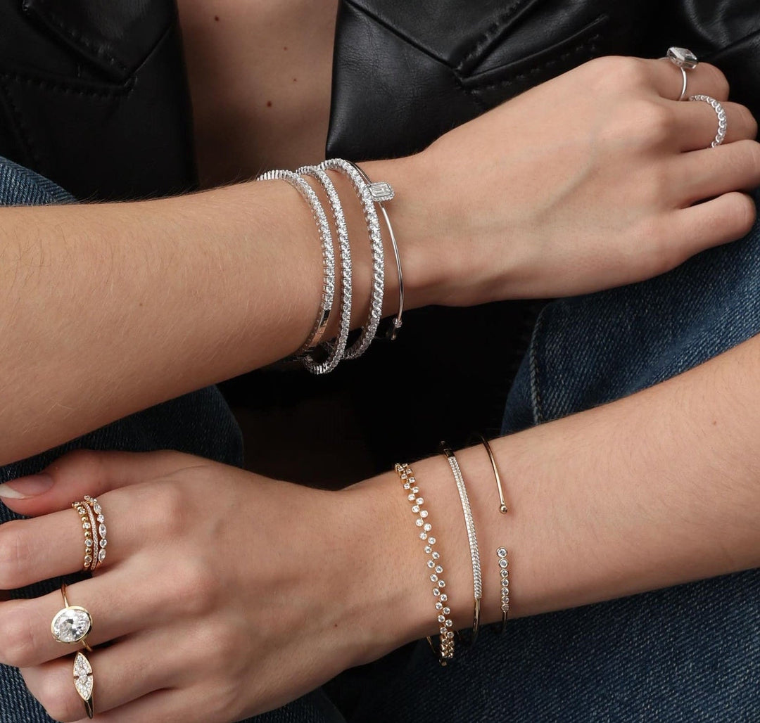 Close-up of a person's arms wearing multiple bracelets and rings on a dark background