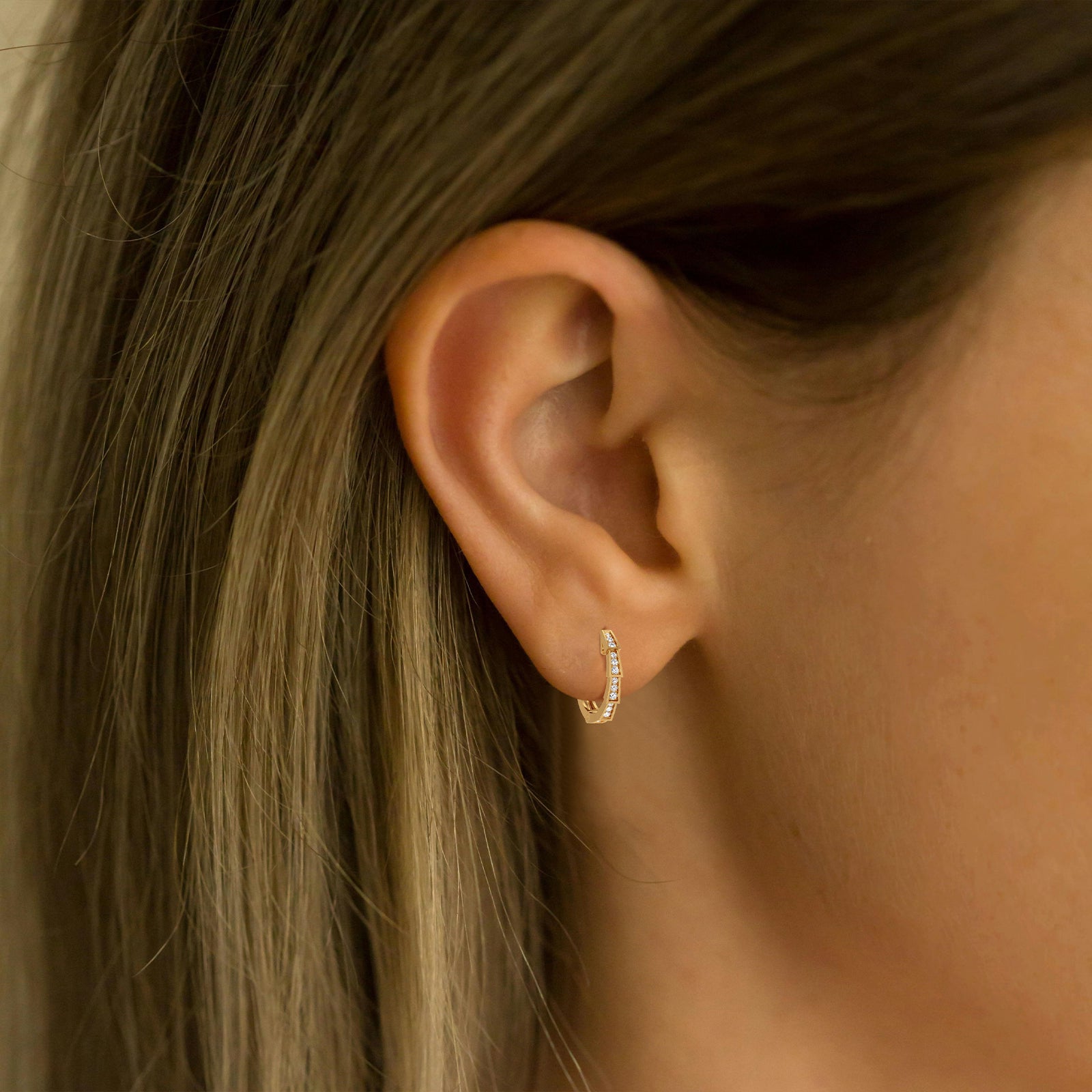 Close-up of an ear wearing a gold hoop earring with hair partially covering the face.