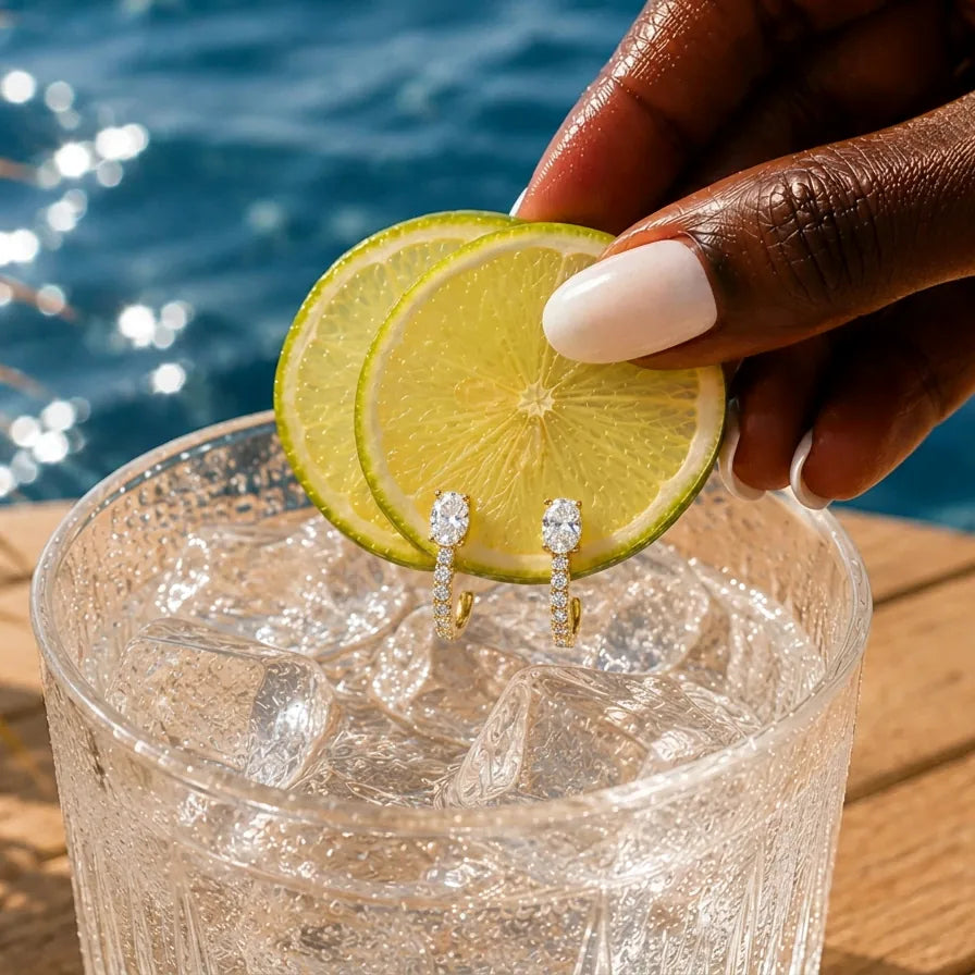 Clear glass with ice and lemon slices, hand holding earrings, blue water background
